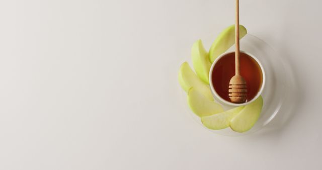 Illustrates a bowl of honey with a wooden dipper surrounded by green apple slices on a white background. Ideal for promoting healthy eating, traditional recipes, or holiday food preparation. Can be used for websites, blogs, or advertisements focusing on natural ingredients, nutritious snacks, or cultural celebrations.