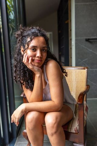 Serene african american woman sitting on rattan chair by window resting chin on hand