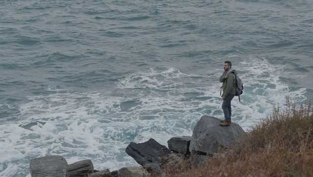 Solitary hiker standing on rocky coast overlooking churning ocean waves and foam
