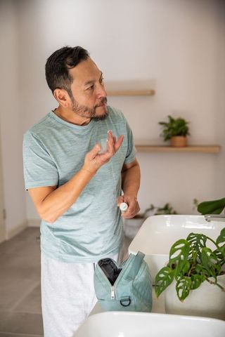 Senior asian man applying facial cream in morning grooming routine in minimalist bathroom