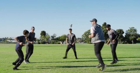 Diverse male teammates practicing rotating passes with red ball on grassy field during warm-up