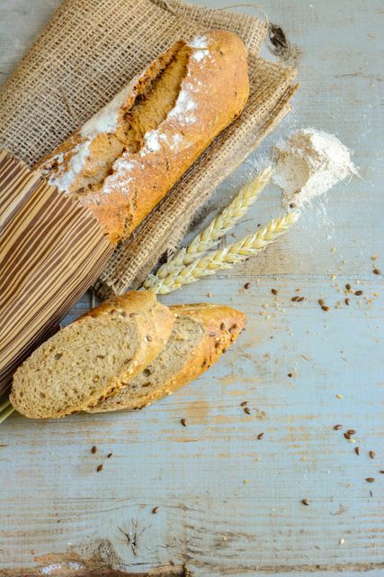 Freshly baked rustic bread placed on burlap next to wheat stalks and sprinkled flour. Perfect for food blogs, bakery websites, organic food promotions, and healthy eating advertisement materials.