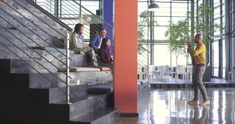 Multicultural team collaborating in sunlit atrium with presenter gesturing at orange column