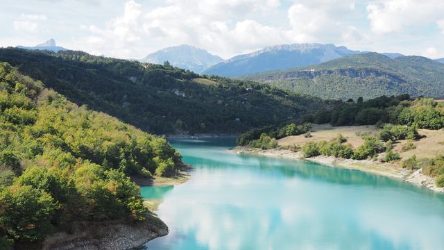 Tranquil Turquoise River Amidst Lush Green Trees With Mountains In Background - Download Free Stock Photos Pikwizard.com