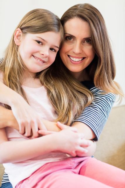 Image of a mother and daughter embracing while smiling in a living room. Ideal for use in family-related articles, advertisements, and social media posts emphasizing family bonds, love, and happiness. Great for parenting magazines, family therapy promotions, and home decor catalogs.