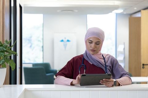 African nurse wearing hijab reviewing patient records on tablet at clinic reception
