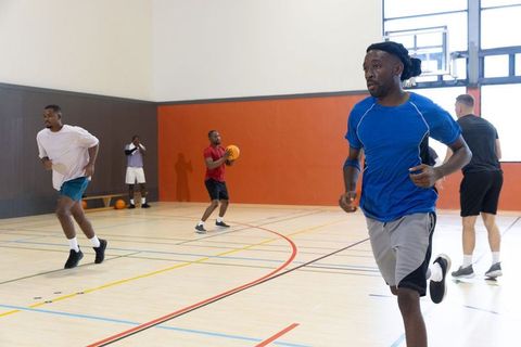 Diverse male players running and passing on indoor basketball court for team practice