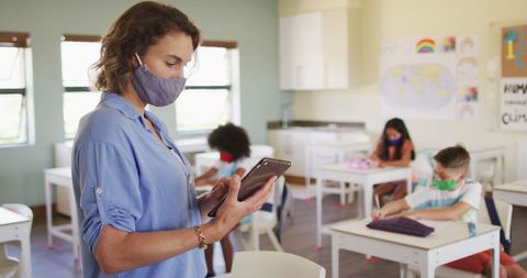 Teacher Using Tablet in Classroom Wearing Face Masks During Pandemic