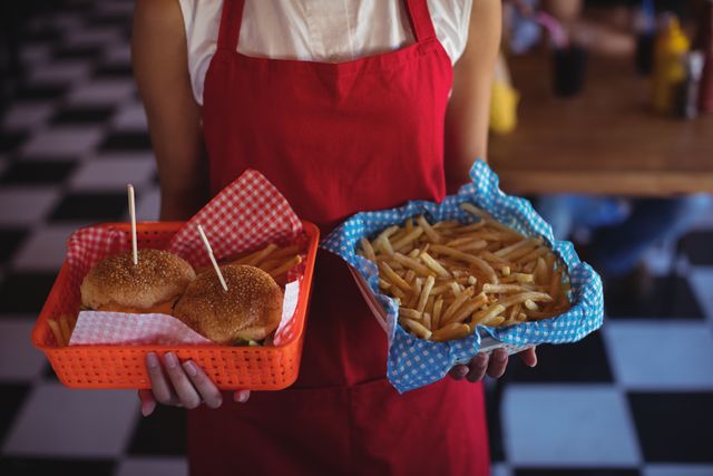 Waitress holding trays with burgers and fries in a retro diner with checkered floor. Ideal for use in advertisements for restaurants, fast food promotions, or articles about American cuisine and dining experiences.
