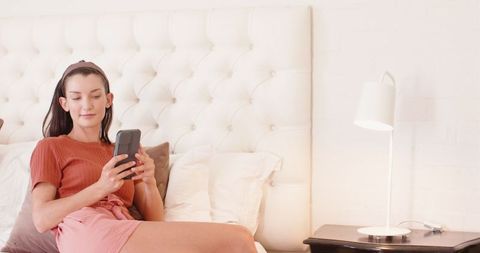 Relaxed woman using smartphone in cozy bedroom