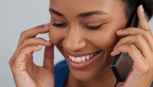 Smiling woman using corded handset, close-up headshot with manicured nails and blue top