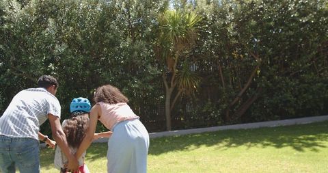 Parents Teaching Daughter to Ride Bike in Sunny Backyard