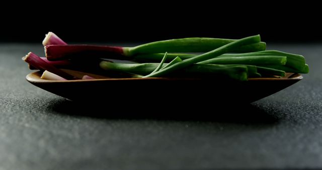 A plate of fresh green onions is presented on a dark background, with copy space. Its simplicity emphasizes the importance of fresh ingredients in culinary presentations.