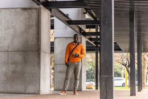 African american man standing beneath steel canopy at urban campus holding coffee