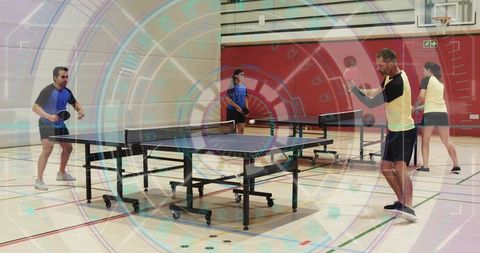 Four players playing doubles table tennis in school gym with foldable tables and paddles