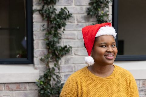 African american woman smiling in santa hat and mustard sweater on brick facade with ivy
