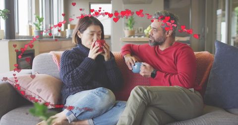 Relaxed couple with heart shapes drinking coffee at home