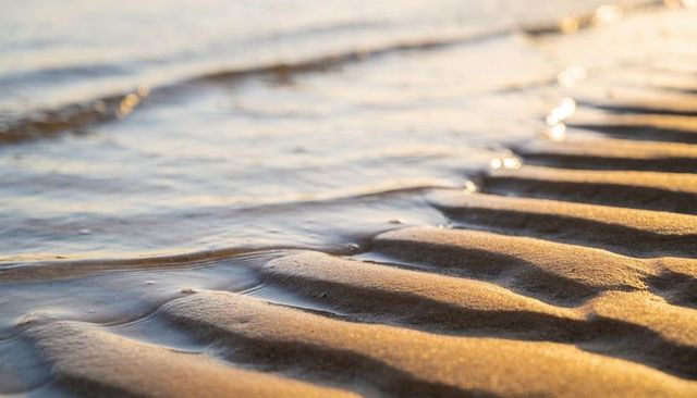Golden hour wet sand ripples shimmering with shallow tide pools on shoreline