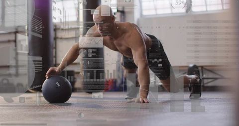 Muscular athlete holding medicine ball reaching on gym floor training with digital data overlays