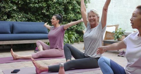 Mature women stretching and laughing on backyard patio during outdoor yoga session