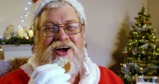A Caucasian senior man dressed as Santa Claus enjoys a cookie, with copy space. His cheerful expression and the Christmas tree in the background evoke the festive spirit of the holiday season.