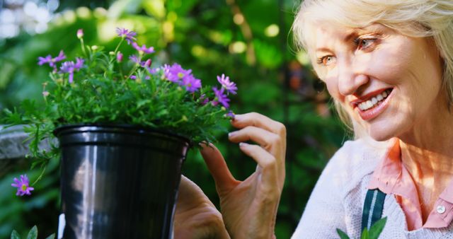 Senior woman smiling while tending to flowers in an outdoor garden, enjoying the sunshine. Ideal for themes on healthy aging, gardening as a hobby, outdoor activities, relaxation, happiness, and nature enjoyment.