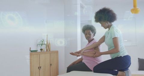 Therapist guiding senior through arm rehabilitation on clinic table with digital hud overlays