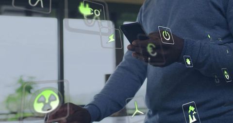 Senior man holding smartphone interacting with ar sustainability and energy icons at office desk