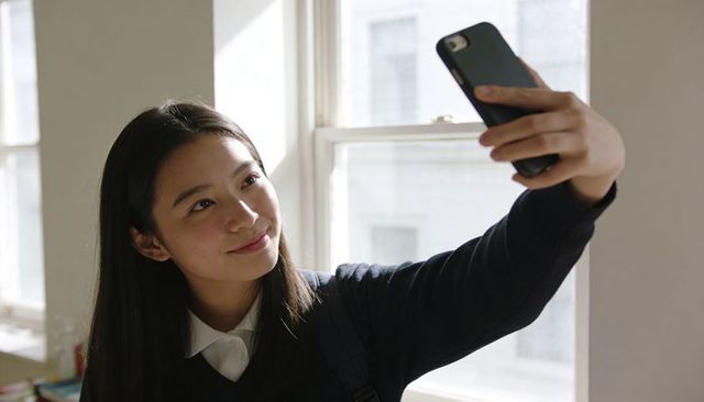 Teen student taking selfie by classroom window with backpack and natural light candid
