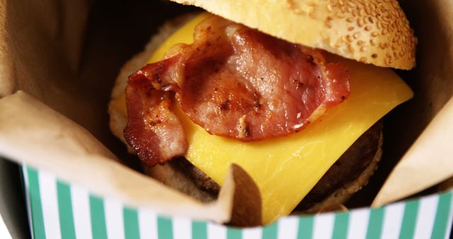 A close-up view of a bacon cheeseburger in a takeout container, showcasing the juicy patty, melted cheese, and crispy bacon. Its presentation in a fast-food style box suggests a quick and satisfying meal option for those on the go.