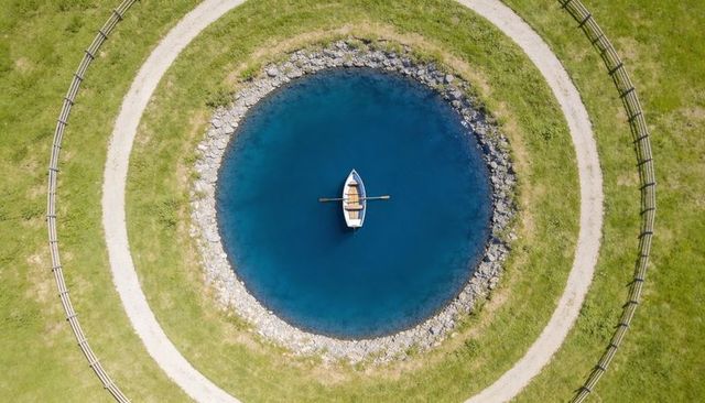 Rowboat floating in perfect concentric pond surrounded by circular paths and green lawn