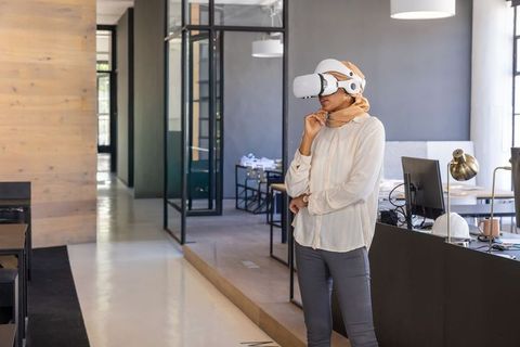 Indian businesswoman wearing hijab using vr headset in modern open-plan office workspace