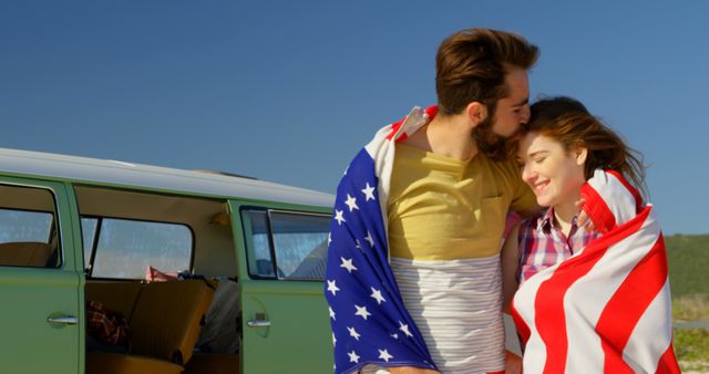 Happy man kissing woman forehead at beach on a sunny day. Couple wrapped with american flag 4k