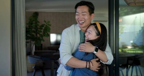 Laughing couple hugging by patio sliding doors wearing denim jacket and smartwatch