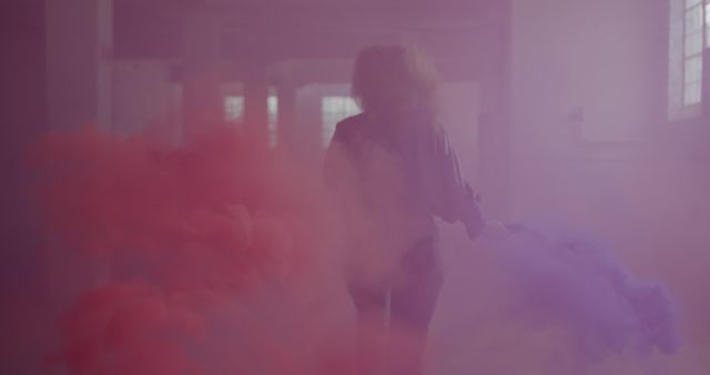 Young Caucasian woman surrounded by vibrant smoke, with copy space. She creates a dynamic atmosphere in an indoor setting with colorful smoke bombs.