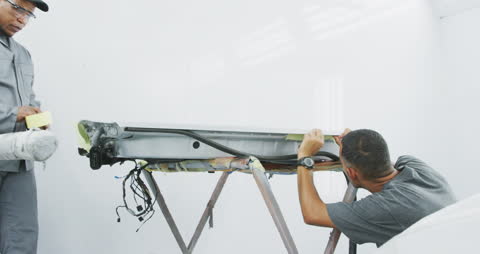Car Mechanics Applying Tape to Vehicle Component in Workshop