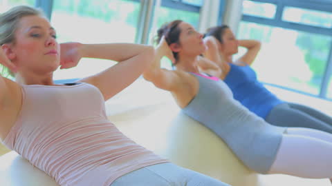 Three Women Performing Sit-Ups on Exercise Balls in Gym