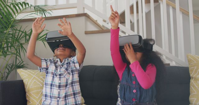 Two children are sitting on a couch in a living room, enthusiastically using virtual reality headsets. They are interacting with virtual content, with one child raising hands and another pointing, indicating immersion and excitement. This can be used in articles and advertisements about virtual reality technology, childhood experiences, gaming, and modern educational tools.