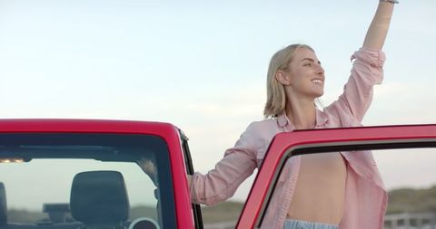 Young Woman Enjoys Freedom Outdoors Next to Red Car on Road Trip