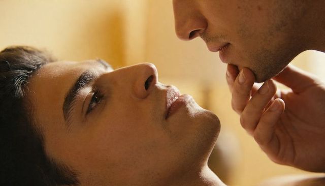 Male couple sharing tender chin touch in warm bedroom closeup