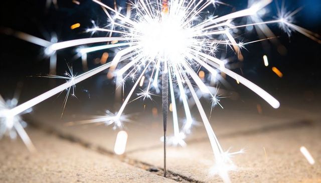 Sparkler emitting bright white sparks over pavement seam at night, closeup celebration