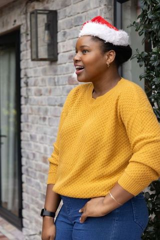 African american woman wearing santa hat and mustard sweater smiling on porch