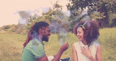 Joyful couple exchanging keepsake in sunlit meadow with dotted world map overlay