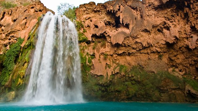 Capturing the mesmerizing sight of a majestic waterfall cascading into a turquoise pool against a backdrop of rugged cliffs. Ideal for travel brochures, nature magazines, and websites promoting natural attractions or serene vacation spots.