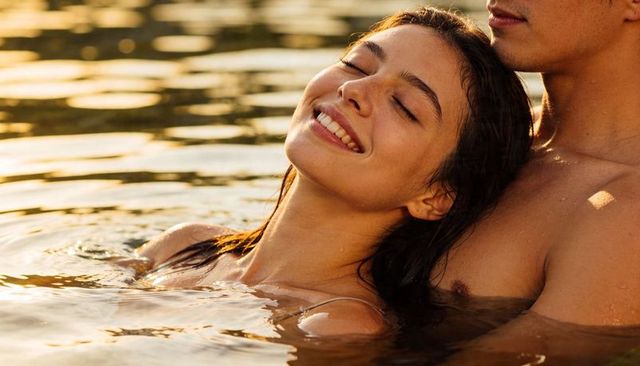 Couple embracing at golden hour on lake, woman relaxing against partner, romantic sunset