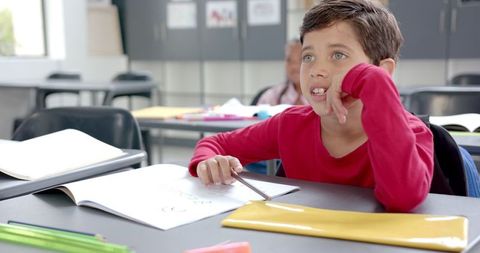 Thoughtful Child Drawing in Classroom with Pencils and Supplies