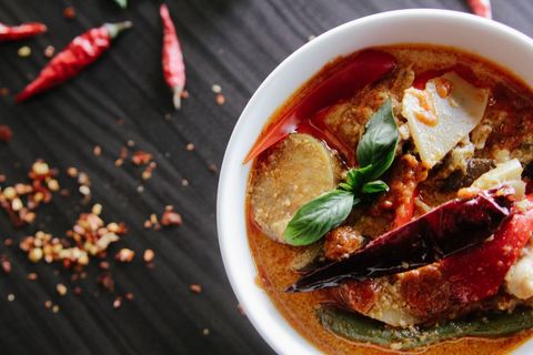 Simmering spicy thai red curry with basil and chilies in white bowl over dark wood surface