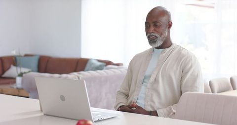 Senior african american man using laptop in modern living room for remote work