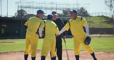 Veteran baseball players greeting umpire at home plate on sunlit field in yellow uniforms