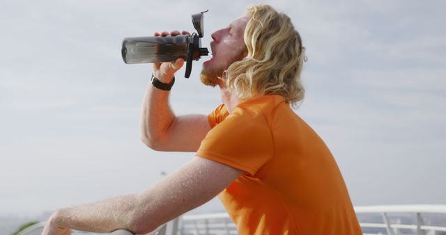 Profile of caucasian man drinking water on bridge in city. Sports, fitness, healthy living and outdoor activities, unaltered.